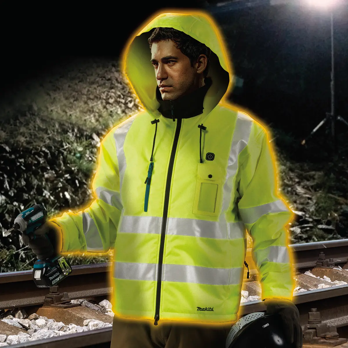 Worker wearing the Makita high visibility heated jacket at night beside railway tracks